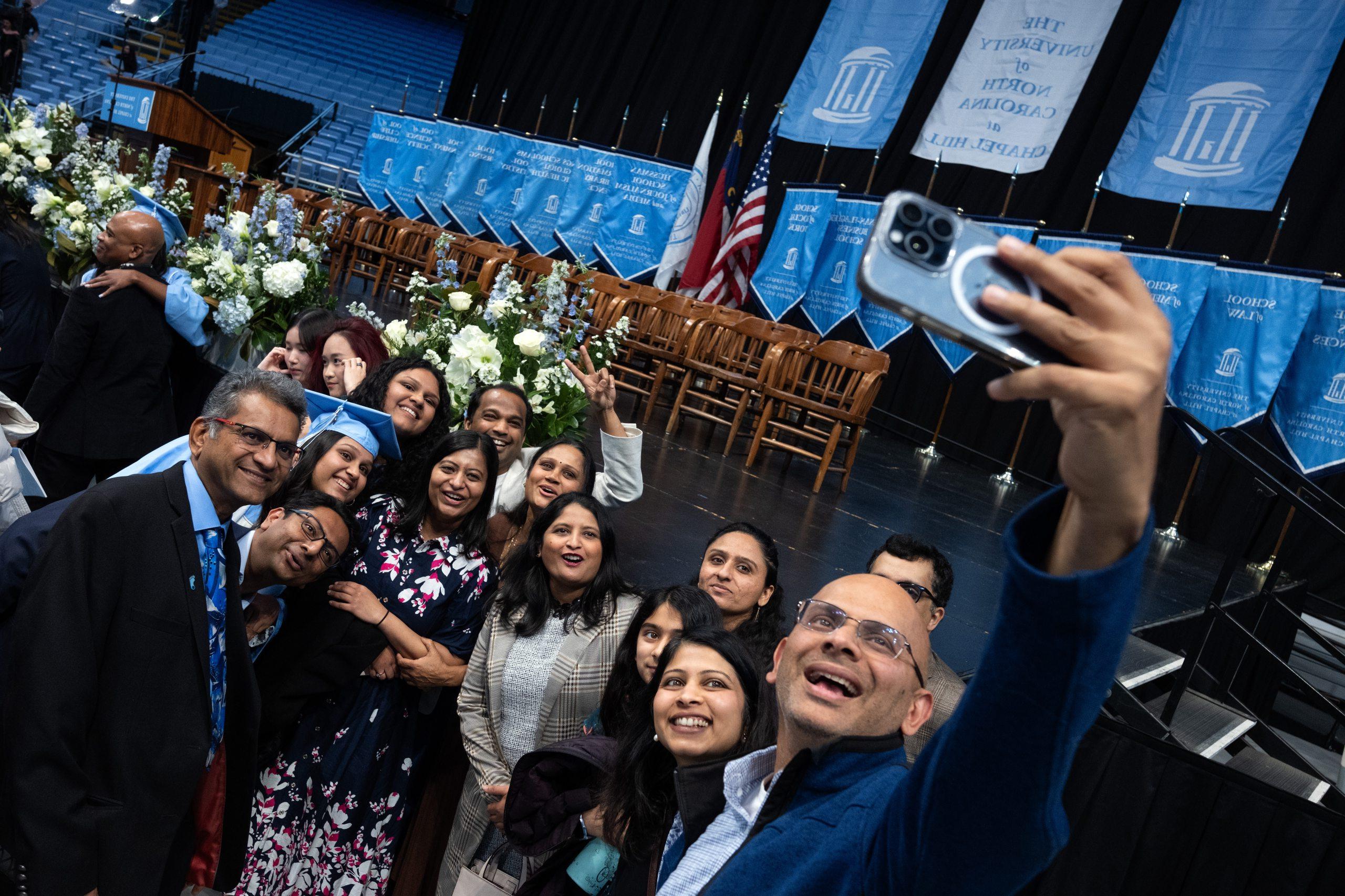 A graduate surrounded by her family, including one man who's taking a group selfie on a phone at U.N.C. Chapel Hill's Winter Commencement.